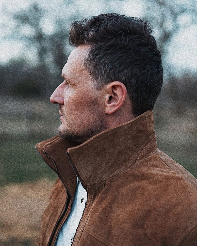 Alex Bond in profile, wearing a suede jacket outdoors